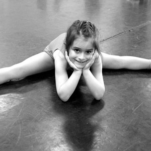 A child dancer is doing the split and smiling